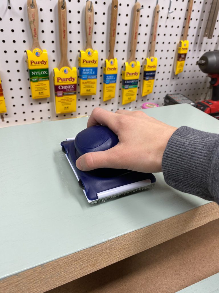 Removing excess solid color stain with a synthetic pad on blue bench